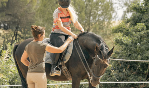 woman helping another person ride a horse in a sunny outdoor setting focusing on horse riding skills and lessons with emphasis on safe riding techniques and six key principles of horsemanship