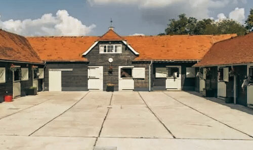 farm building with red roof surrounding courtyard featuring two side structures and a central entrance showcasing 7 horse stalls and clear outdoor space